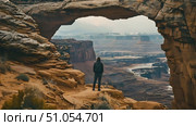 Hiker man stands on a cliff, overlooking the vast desert landscape below. He gazes out at the arid expanse, taking in the rugged beauty of the terrain. Стоковое AI-видео, аниматор Данила Большаков / Фотобанк Лори