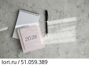 Notebook with "2026" written on it and pen, placed on light gray textured background. Top-down view is ideal for themes of planning, goal-setting and new year resolutions. Стоковое фото, фотограф Елена Никишина / Фотобанк Лори