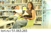 Group of students reading and discussing books while sitting on chair in library. Стоковое видео, видеограф Яков Филимонов / Фотобанк Лори