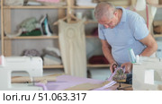 Mature man cutting fabric with tailoring scissors. Cutter, after selecting the fabric, makes an incision. Process of creating clothes according to individual measurements. Стоковое видео, видеограф Яков Филимонов / Фотобанк Лори