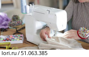 Close-up of professional female seamstress hands working at sewing machine, stitching checkered fabric with focus and precision at table in workshop. Стоковое видео, видеограф Яков Филимонов / Фотобанк Лори