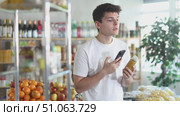 Before buying smoothie, young man scans barcode QR code on label of smoothie package bottle, follows link and studies information for consumer in supermarket application. Стоковое видео, видеограф Яков Филимонов / Фотобанк Лори
