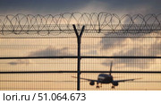 Airplane landing behind airport fence with barbed wire at sunset. Стоковое видео, видеограф Mikhail Davidovich / Фотобанк Лори