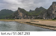 There are shallow puddles on the pebbly riverbank. Picturesque coastal cliffs with steep slopes and green vegetation. Clouds in the sky. The riverbed is in the foreground. China. Li River. Li Jiang. Стоковое фото, фотограф Вера Ивановна Кубарева / Фотобанк Лори
