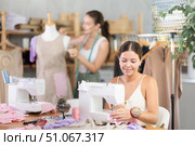 Young tailoress using sewing-machine while other working with mannequin. Стоковое фото, фотограф Яков Филимонов / Фотобанк Лори