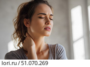 Красивая молодая девушка, держащаяся руками за шею от боли, стоит в ярком современном интерьере. Стоковое AI-изображение, AI-художник Максим Коломыченко / Фотобанк Лори