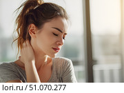 Красивая молодая девушка, держащаяся руками за шею от боли, стоит в ярком современном интерьере. Стоковое AI-изображение, AI-художник Максим Коломыченко / Фотобанк Лори