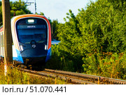 The train is surrounded by trees and grass, it is a commuter train. Russia. Moscow oblast. 14.08. 2025. Редакционное фото, фотограф Ярославский Максим / Фотобанк Лори