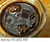 A close-up of a jar of pine cone jam, clearly showing the small young pine cones submerged in a thick, dark amber syrup. The shiny surface of the syrup reflects the light, creating a delicious and inviting appearance. You can see how the seeds and texture of the pine cones contrast with the smooth consistency of the sweet liquid. Pine cone jam is known for its rich, pine-like aroma and health benefits - it is often used as a treat and as a natural remedy for supporting the immune system. The image is perfect for illustrations of recipes, publications on canning, cooking, traditional medicine and natural products. Стоковое фото, фотограф Анна Кривицкая / Фотобанк Лори
