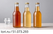 Three glass bottles of kombucha showing different fermentation stages and a glass. Стоковое AI-изображение, AI-художник Юрий Поздников / Фотобанк Лори