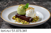 Delicious pistachio and vanilla ice cream scoops topping chocolate fudge cake slice. Стоковое AI-изображение, AI-художник Юрий Поздников / Фотобанк Лори