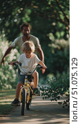Father helps son learn to ride a bicycle in a park during summer afternoon surrounded by greenery. Стоковое AI-видео, аниматор Сергей Толмачёв / Фотобанк Лори