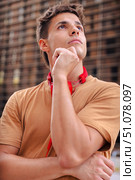 Young man in brown t-shirt with red headphones thinking outdoors in the city. Стоковое фото, фотограф Raquel Corcoles Mendez / Фотобанк Лори