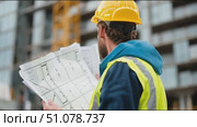 Construction worker reviews plans on a building site with a crane in the background during daylight hours. Стоковое AI-видео, аниматор Сергей Толмачёв / Фотобанк Лори