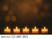 Five lit candles in glass holders on a dark background. The warm glow creates a serene atmosphere, symbolizing remembrance and honoring ancestors during Día de los Muertos. Стоковое AI-изображение, AI-художник Nart / Фотобанк Лори