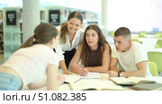 Group of student sits at table in library and studies, reads books and takes notes. Стоковое видео, видеограф Яков Филимонов / Фотобанк Лори