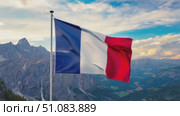French flag waving in the wind against a mountainous landscape. The sky is partly cloudy, showcasing a serene natural setting. Стоковое AI-видео, аниматор Nart / Фотобанк Лори