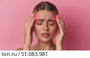Young Caucasian woman with long brown hair holds her head in pain against a pink background. She appears distressed, indicating a headache or discomfort. Стоковое AI-видео, аниматор Nart / Фотобанк Лори
