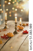A rustic wooden table adorned with small orange pumpkins, colorful autumn leaves, and lit candles. Soft bokeh lights create a warm, inviting atmosphere. Стоковое AI-видео, аниматор Nart / Фотобанк Лори