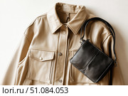 Beige leather jacket with zippers and pockets and black leather stylish bag. Modern outerwear. Close-up. Fashion background. Autumn urban street clothes. Fashionable concept. Women's casual day outfit. Стоковое AI-изображение, AI-художник Марина Демидюк / Фотобанк Лори