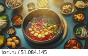 A hot pot meal with various ingredients including meat, vegetables, and seafood arranged around a central pot. Steam rises from the pot, creating a warm atmosphere. Стоковое AI-видео, аниматор Nart / Фотобанк Лори
