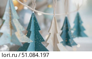 Colorful paper Christmas tree decorations hang on a string. The trees are in shades of blue and white, adorned with glitter. Soft bokeh lights are in the background. Стоковое AI-видео, аниматор Nart / Фотобанк Лори