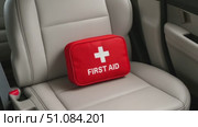 A red first aid kit with a white cross sits on a beige car seat. The kit is compact and designed for emergency medical supplies. Стоковое AI-видео, аниматор Nart / Фотобанк Лори