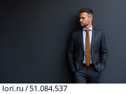 Caucasian businessman in a formal wear isolated on a dark gray background. Confident man in suit standing over black wall. Business concept. Mature executive manager, proud lawyer, successful leader. Стоковое AI-изображение, AI-художник Марина Демидюк / Фотобанк Лори