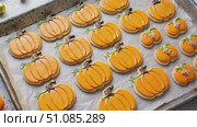 A tray of decorated pumpkin-shaped cookies in vibrant orange icing. The cookies are arranged neatly on parchment paper, showcasing a festive Halloween theme. Стоковое AI-видео, аниматор Nart / Фотобанк Лори