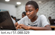 An African boy working on a school project in a tech-equipped classroom, using a laptop and educational software. Black African children from disadvantaged families study in school, read books, receive primary education, volunteer service. Стоковое AI-изображение, AI-художник ALLA YURTAYEVA / Фотобанк Лори
