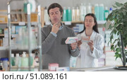 Careful middle-aged male client holding pack of medical preparation and apothecary consulting him in drugstore. Стоковое видео, видеограф Яков Филимонов / Фотобанк Лори