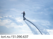 A man in a black athlete wetsuit hovers against a dramatic sky on a flyboard. flyboard enthusiast performs impressive aerial tricks above the water, propelled by powerful jets beneath their feet. Стоковое фото, фотограф Владимир Разгуляев / Фотобанк Лори