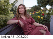 Woman in a rose dress sits on a bench near blooming hydrangeas, gazing thoughtfully into the distance with a serene expression. Стоковое фото, фотограф Софья Соломонова / Фотобанк Лори
