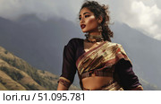 Elegant woman in traditional attire poses against a mountain backdrop during daylight. Стоковое AI-изображение, AI-художник Ксения Лаптева / Фотобанк Лори