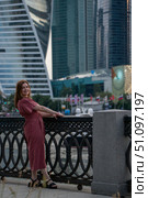 Woman in a red dress leaning on a decorative railing with skyscrapers of Moscow City in the background. Редакционное фото, фотограф Софья Соломонова / Фотобанк Лори