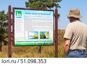 KHOLMUSHINO VILLAGE, IRKUTSK REGION, RUSSIA - August 15, 2025: A tourist reads an information banner about the natural landmark of the White rocks on the Belaya River on summer sunny day. Редакционное фото, фотограф Виктория Катьянова / Фотобанк Лори
