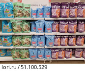 A rack in a pet store or supermarket with a large selection of cat litter. The shelves are lined with packages of different brands and colors. On the left are blue 8-liter Pretty Cat packages, in the center are light green 6-liter Cat Step Tofu Green Tea packages and blue CC Cat packages, on the right are purple Cat Step packages with a picture of a ginger cat. The packages are neatly arranged in rows, with price tags under each shelf: from 308 to 512 rubles, depending on the brand and volume. The photo demonstrates the variety of products and the order of their display in the store. (2019 год). Редакционное фото, фотограф Анна Кривицкая / Фотобанк Лори