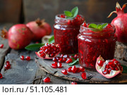 Jars of pomegranate jam decorated with mint leaves and fresh pomegranates on rustic wooden table. Стоковое AI-изображение, AI-художник Иван Рябоконь / Фотобанк Лори