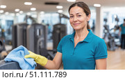 Smiling cleaning woman disinfecting gym equipment with cloth and gloves, promoting hygiene, sanitation, and cleanliness in a professional fitness environment. Стоковое AI-изображение, AI-художник Катерина Бондарец / Фотобанк Лори