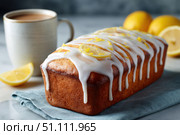 Homemade lemon drizzle cake with icing. Classic lemon pound cake with citrus glaze and zest. Whole loaf, side view, close up. Fresh homemade baked dessert with lemon slices. Blurred tea set background. Стоковое AI-изображение, AI-художник Марина Демидюк / Фотобанк Лори