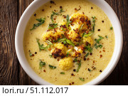 Cauliflower creamy soup with baked cauliflower florets on the top in a white bowl on a dark wood tabletop. Restaurant style dish. Hot, delicious plate of cream-of-cauliflower soup with melted cheese. Стоковое AI-изображение, AI-художник Марина Демидюк / Фотобанк Лори