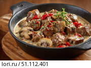 Meat and mushrooms. Dish of stir-fried beef fillet and mushrooms in a creamy thick sauce, served on an iron plate on a wooden board, close-up view. Gourmet food. Beef stroganoff large pieces. Stir Fry. Стоковое AI-изображение, AI-художник Марина Демидюк / Фотобанк Лори