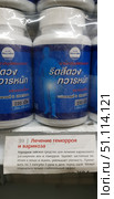 Traditional Thai capsule remedy for the treatment of hemorrhoids and varicose veins. A white plastic jar with a blue label contains 230 capsules of 400 mg. The package depicts a silhouette of a person, which symbolizes the effect on the body. The display case also contains a card with a description in Russian: the remedy helps with varicose veins and hemorrhoids, eliminates congestion in veins and tissues, reduces swelling. It is recommended to take 3 capsules 3 times a day before meals. A mild laxative effect may be observed. The photo is suitable for illustrating topics related to natural remedies, traditional medicine and vascular health products. (2018 год). Редакционное фото, фотограф Анна Кривицкая / Фотобанк Лори