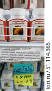 Jars of safflower capsules (Carthamus tinctorius) displayed on a store shelf. The product is manufactured under the brand name Thanyaporn Herbs (Thailand). The packaging depicts a bright yellow-orange safflower flower. Under each jar is a sign with a description in Russian: the product regulates blood sugar levels, increases insulin sensitivity, inhibits inflammation in diabetes and obesity, is used to prevent cardiovascular diseases, and is also prescribed for psoriasis and some gynecological ailments. Price tags and inscriptions in Thai are visible below. The atmosphere of the photo conveys the flavor of an Asian store of natural remedies and traditional medicine. (2018 год). Редакционное фото, фотограф Анна Кривицкая / Фотобанк Лори
