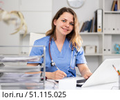 Positive woman doctor sitting at workplace with computer in office. Стоковое фото, фотограф Яков Филимонов / Фотобанк Лори