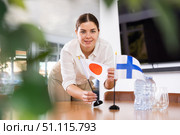 Positive young woman putting flag of Japan on the table with flag of Finland in conference room. Стоковое фото, фотограф Яков Филимонов / Фотобанк Лори