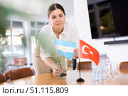 Positive young woman putting flag of Argentina on the table with flag of Turkey in conference room. Стоковое фото, фотограф Яков Филимонов / Фотобанк Лори