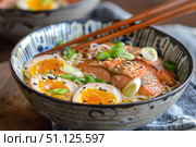 Salmon ramen with soft boiled egg and scallions being enjoyed with chopsticks. Стоковое AI-изображение, AI-художник Иван Рябоконь / Фотобанк Лори