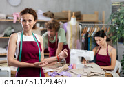 Middle-aged female dressmaker inviting clients while others sew and draw. Стоковое фото, фотограф Яков Филимонов / Фотобанк Лори