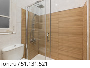 Modern bathroom with a glass shower enclosure and wooden wall panels. White toilet and tiled floor are visible. Bright lighting enhances the clean design. Стоковое фото, фотограф PAv / Фотобанк Лори